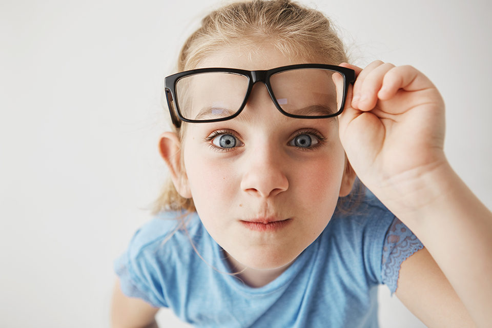 close-up-portrait-of-curious-little-girl-with-big-blue-eyes-standing-close-and-looking-in-camera-holding-glasses-with-hand